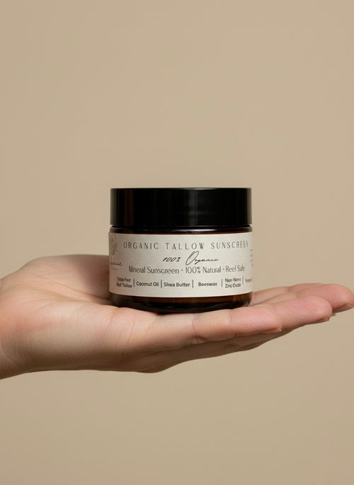 Hand holding a jar of Organic Tallow Sunscreen against a beige background.